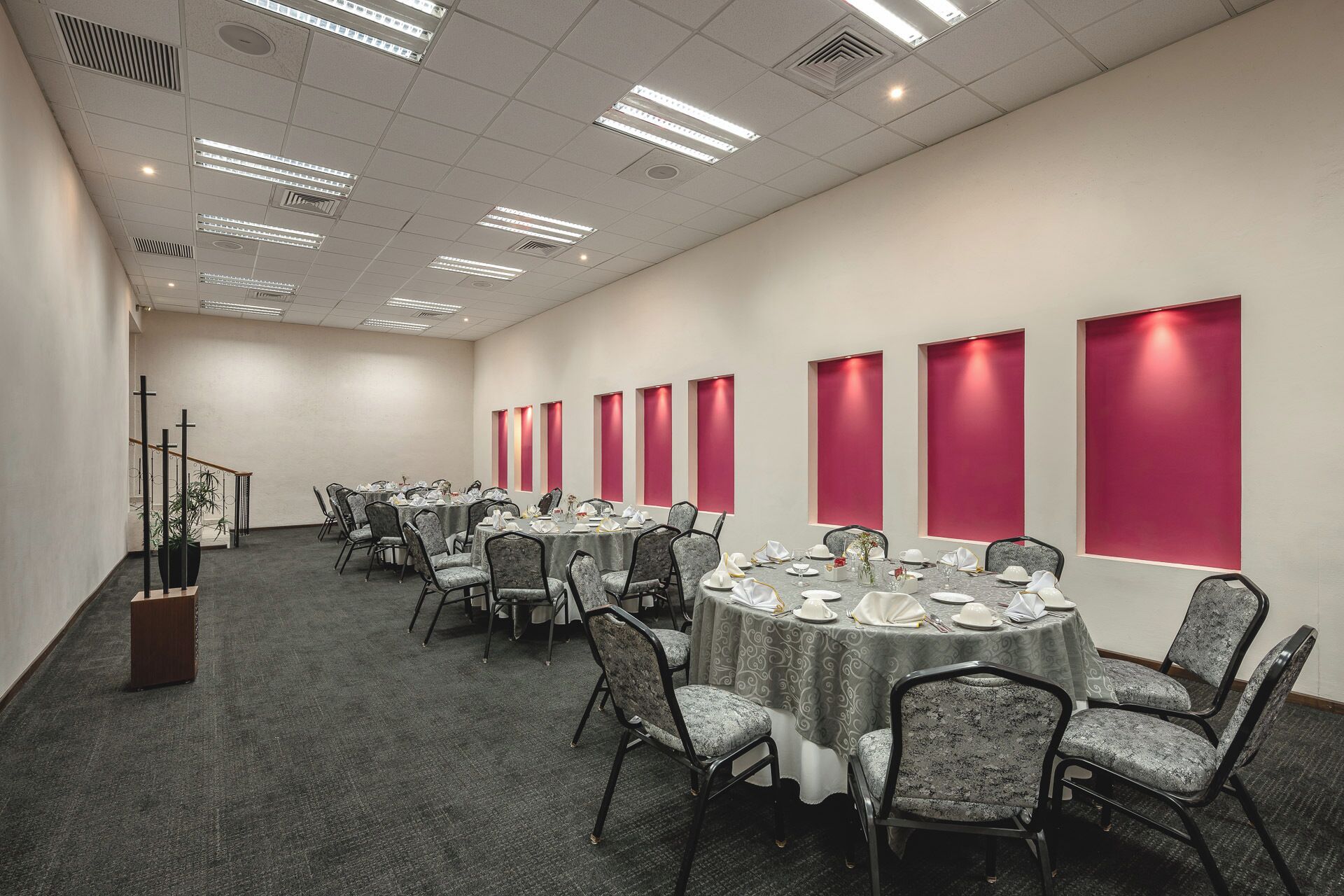 Un salón de conferencias con varias mesas redondas, sillas y piso alfombrado.