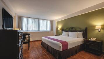 Habitación de hotel con cama, escritorio, silla, televisión y ventana con cortinas.