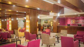 A hotel lobby with multiple seating areas, a reception desk, and a television screen.