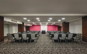 Un salón de conferencias con filas de sillas, una pantalla de proyector y piso alfombrado.