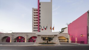 Un hotel con una torre vertical destacada, varios balcones y una fachada de piedra con arcos.