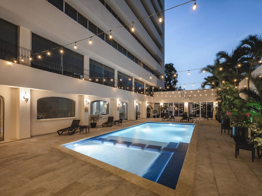 A hotel pool area with a clear pool, lounge chairs, and a covered seating area.
