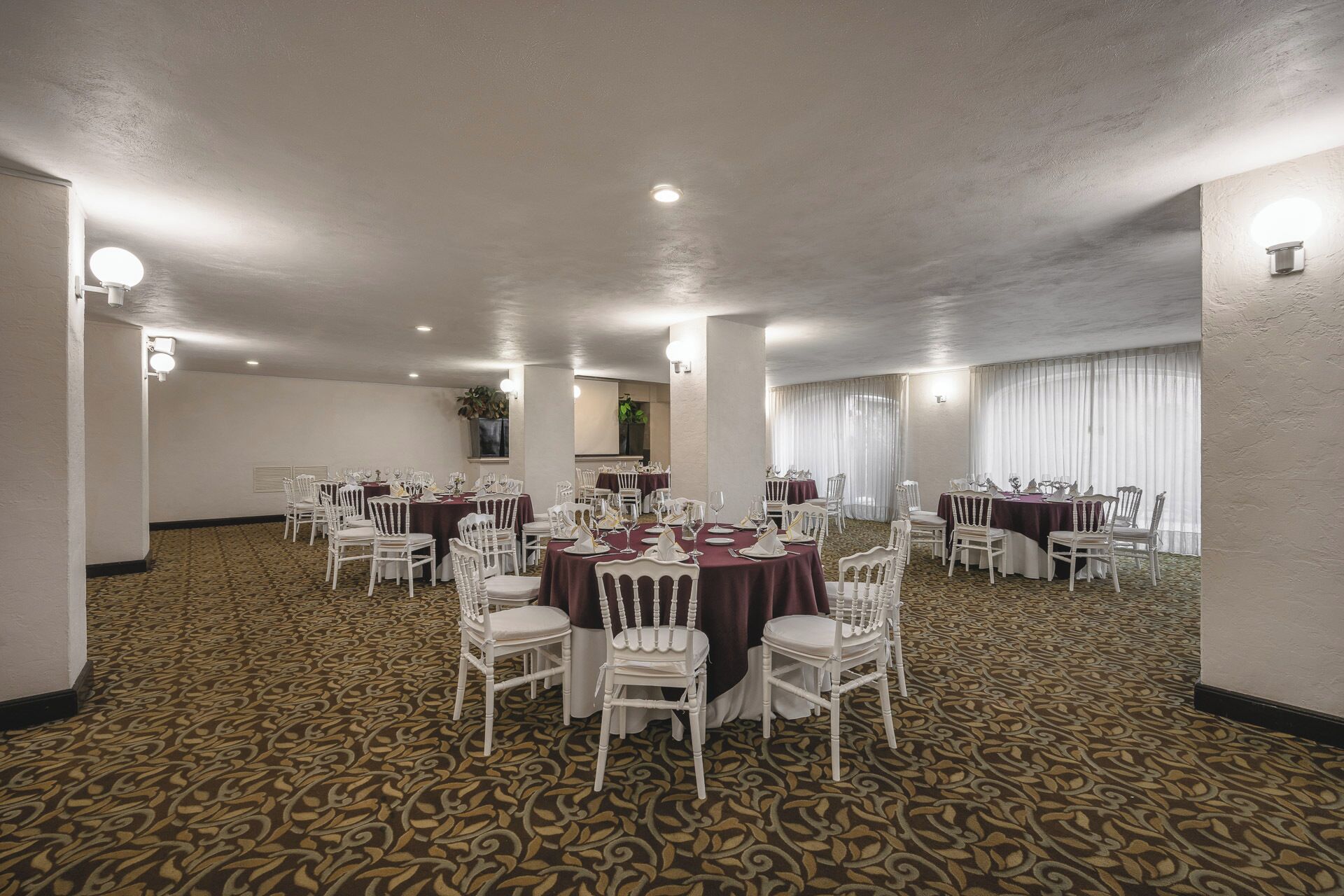 A conference room with multiple tables and chairs, carpeted floor, and ceiling lights.