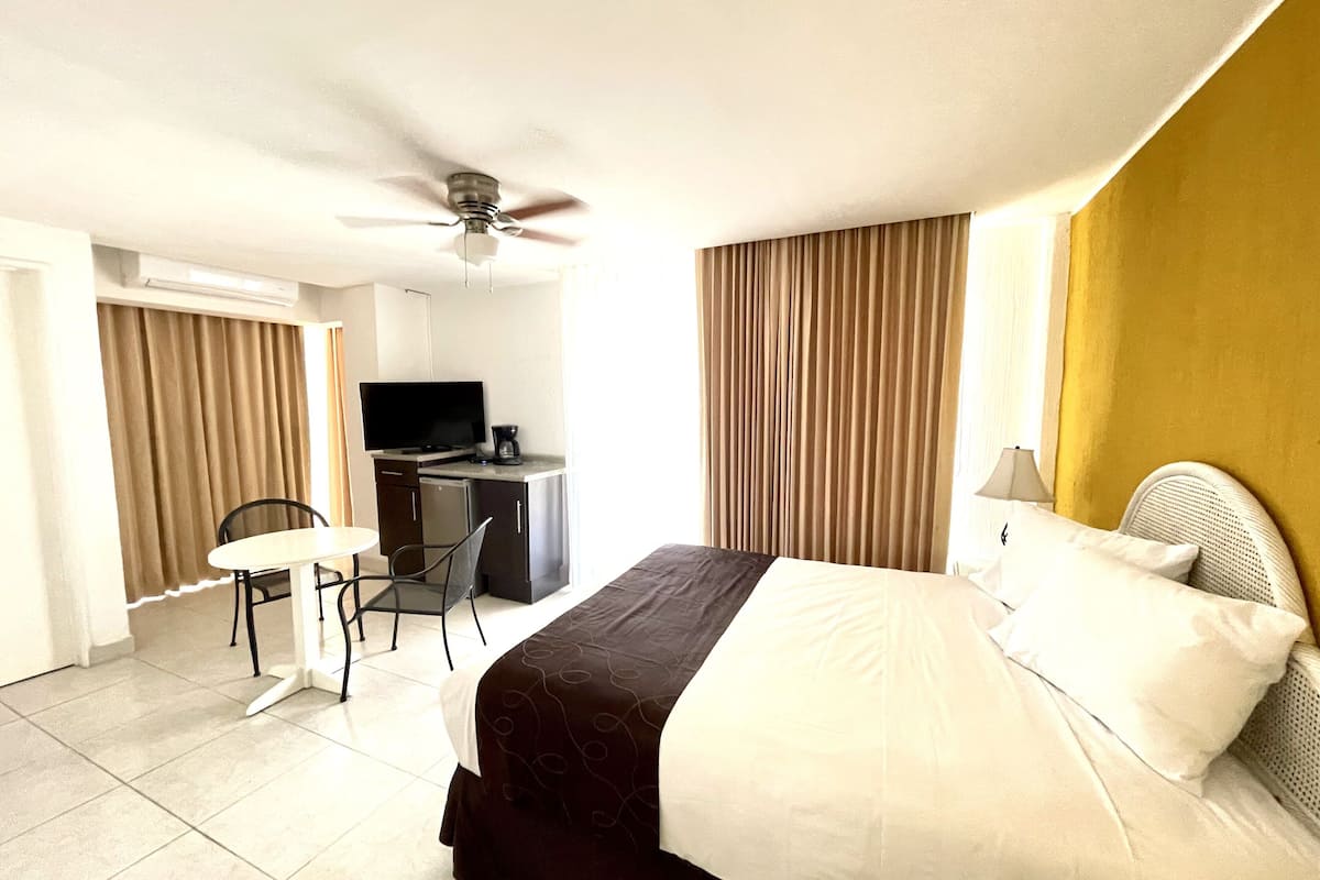 Une chambre d’hôtel comprenant un lit, un bureau avec une télévision, une chaise et un ventilateur de plafond.