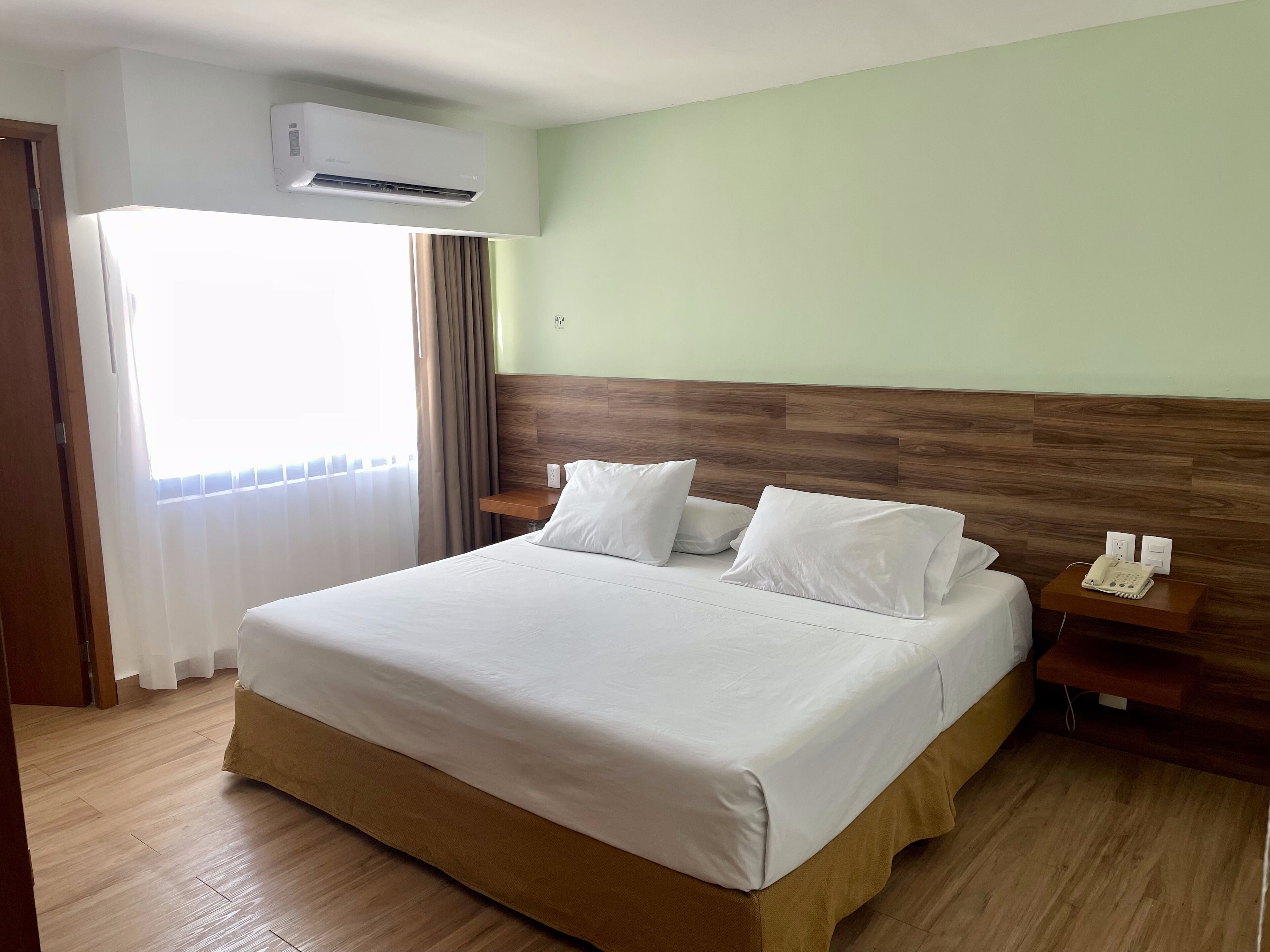 Une chambre d’hôtel avec un grand lit, une tête de lit en bois, des tables de chevet, un climatiseur et un téléphone.