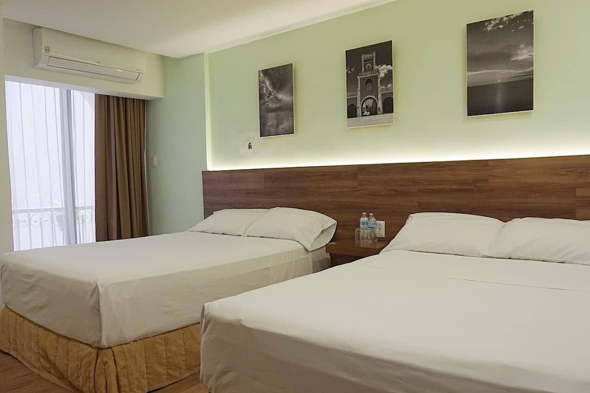 Une chambre d’hôtel avec deux lits, une tête de lit en bois, une fenêtre avec des rideaux et trois tableaux accrochés au mur.