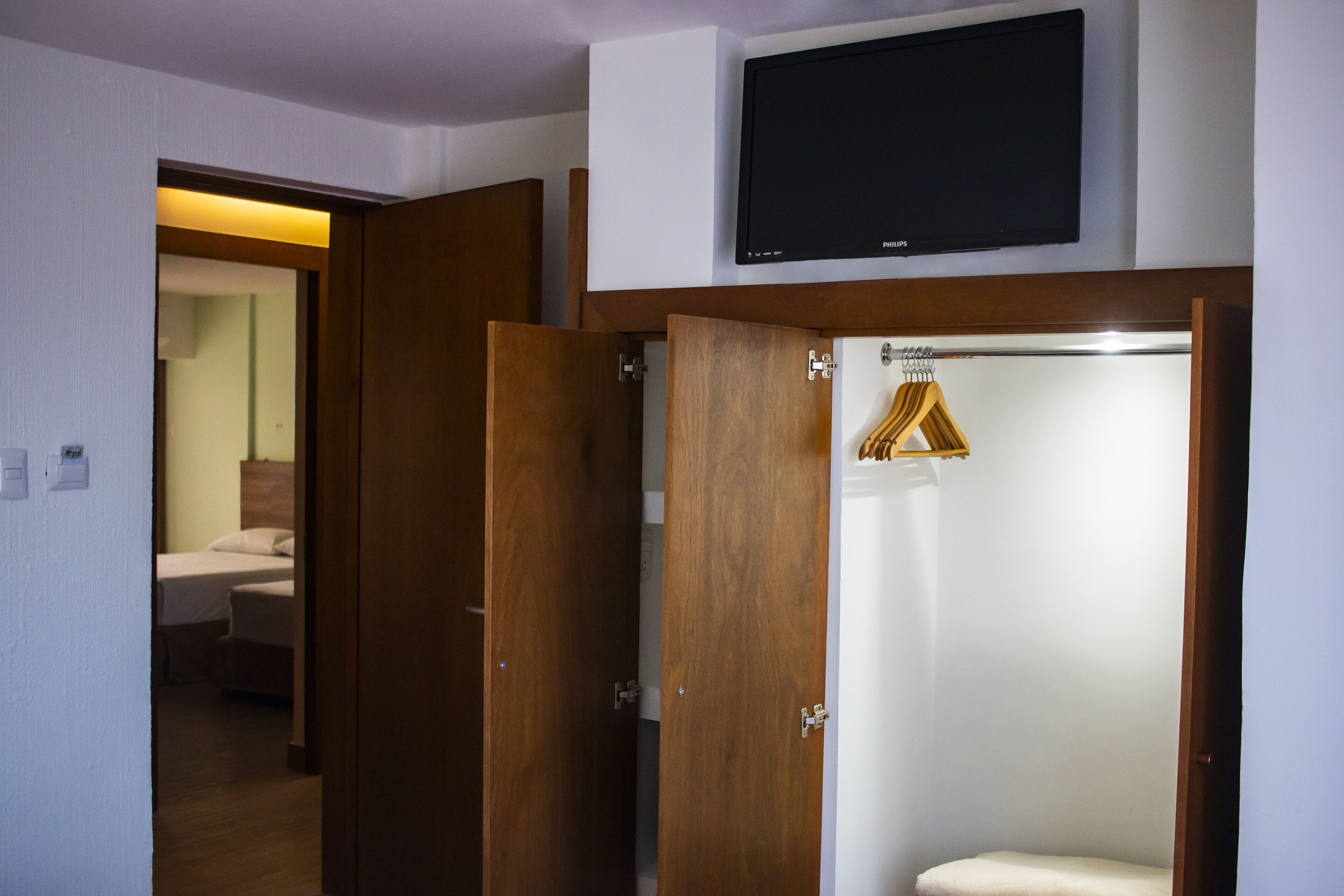 Habitación de hotel con puerta de madera, televisor montado encima de la puerta y baño visible con cortina de ducha.