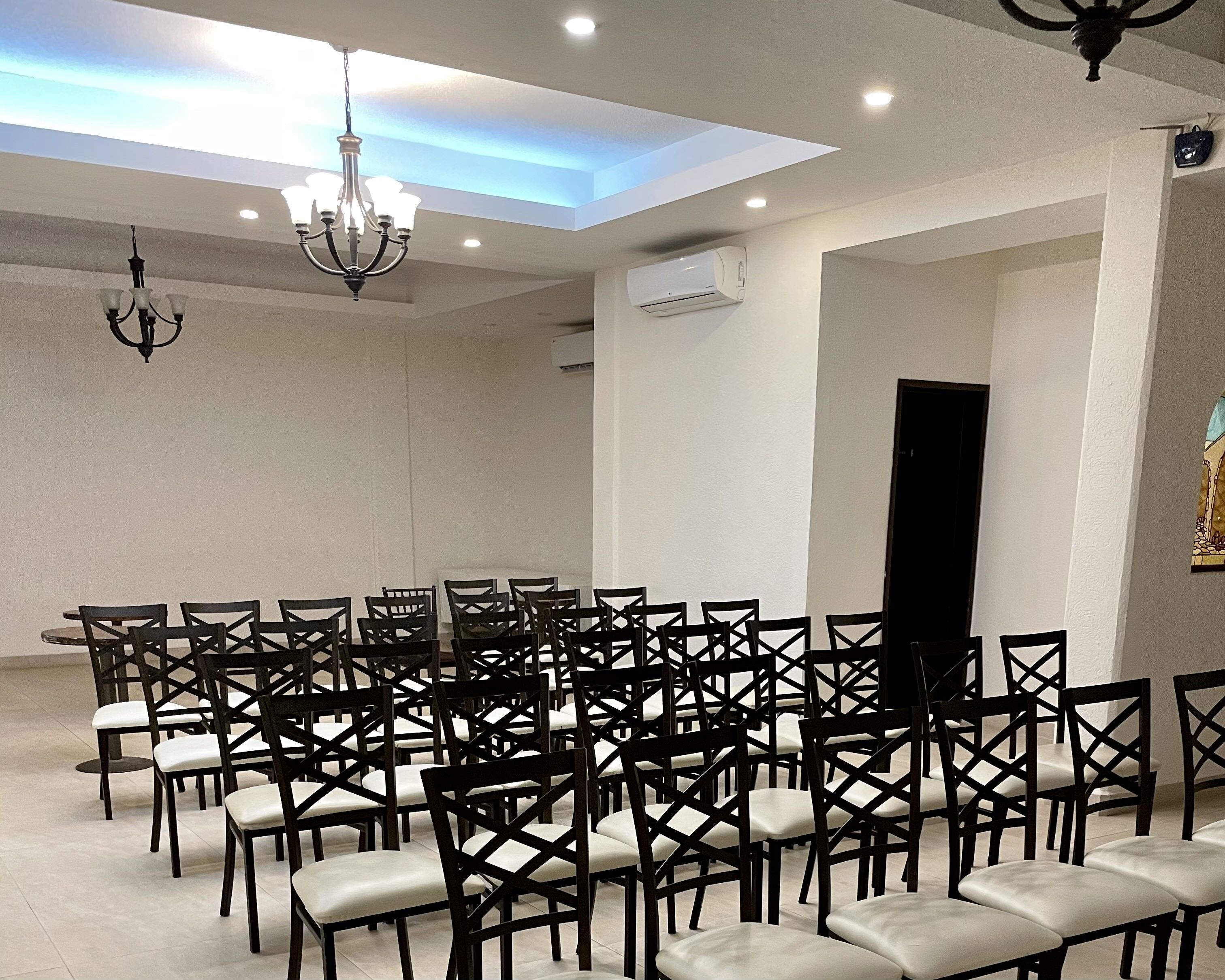 A conference room with rows of chairs, a chandelier, and recessed ceiling lights.