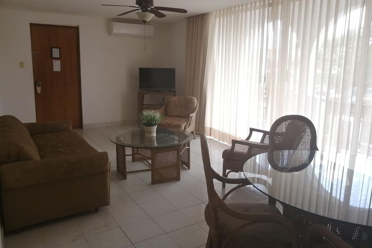 Un salon comprenant un canapé, une table basse en verre, un téléviseur et un ventilateur de plafond.