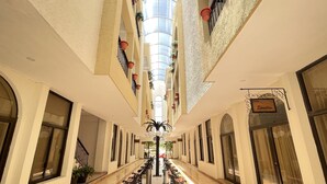A hotel corridor with a central walkway, potted plants, and benches. - Hotel del Paseo Campeche (Campeche)