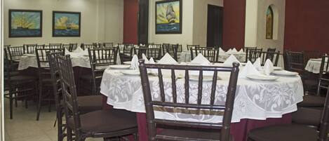 A dining area with multiple tables set for service, chairs arranged around them, and artwork on the walls.
