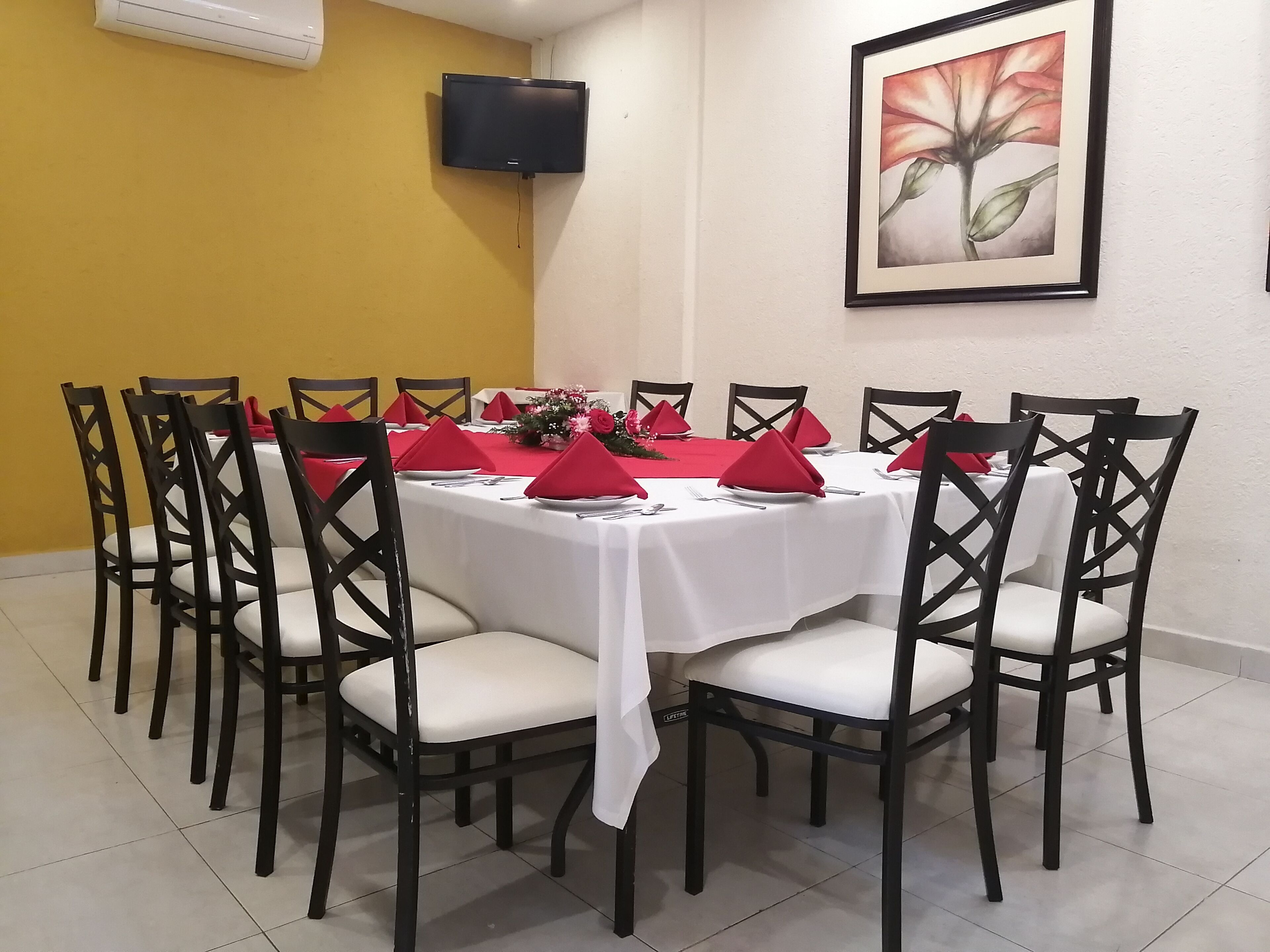 A dining area with a round table, red napkins, white tablecloth, and black chairs.
