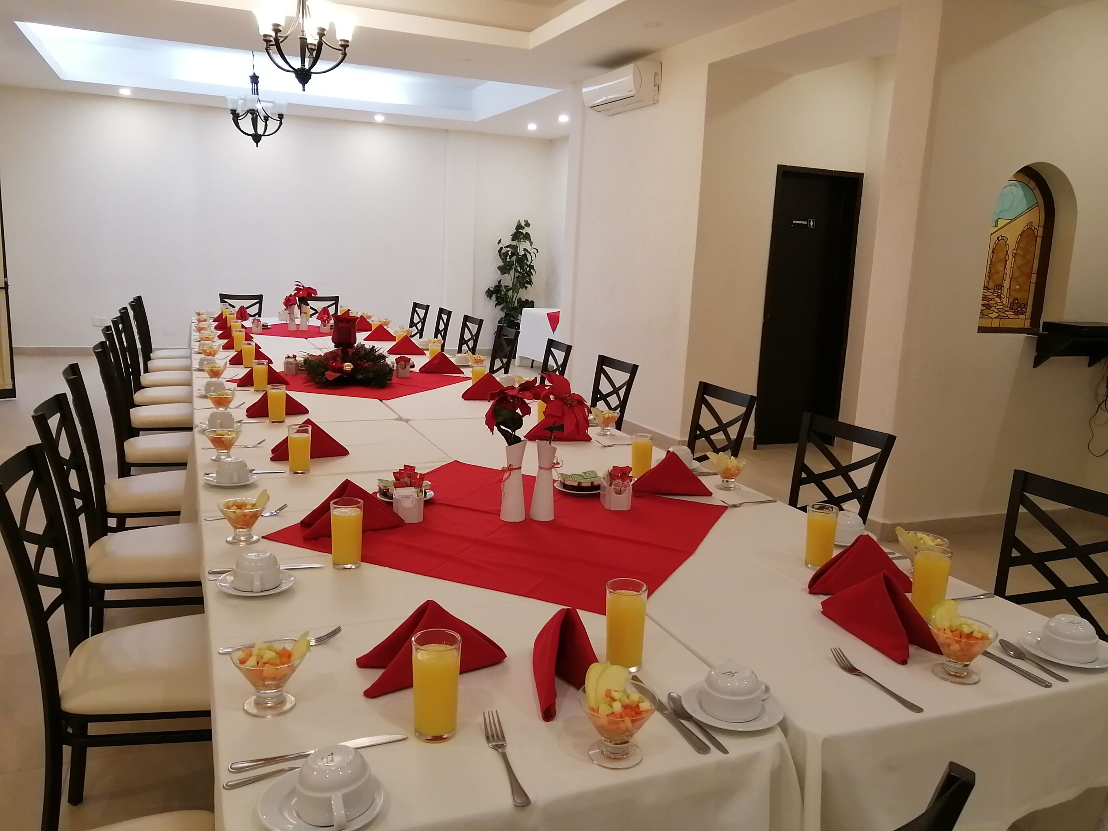 A dining room with a long table set for a meal, featuring red napkins, white tablecloths, and various dishes and drinks.