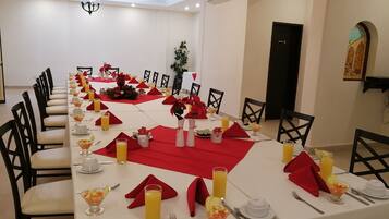 A dining room with a long table set for a meal, featuring red napkins, white tablecloths, and various dishes and drinks.