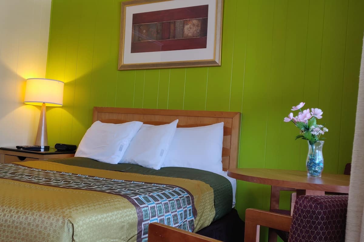 Quarto de hotel com uma cama, mesa de cabeceira, luminária, cadeira e um vaso com flores.