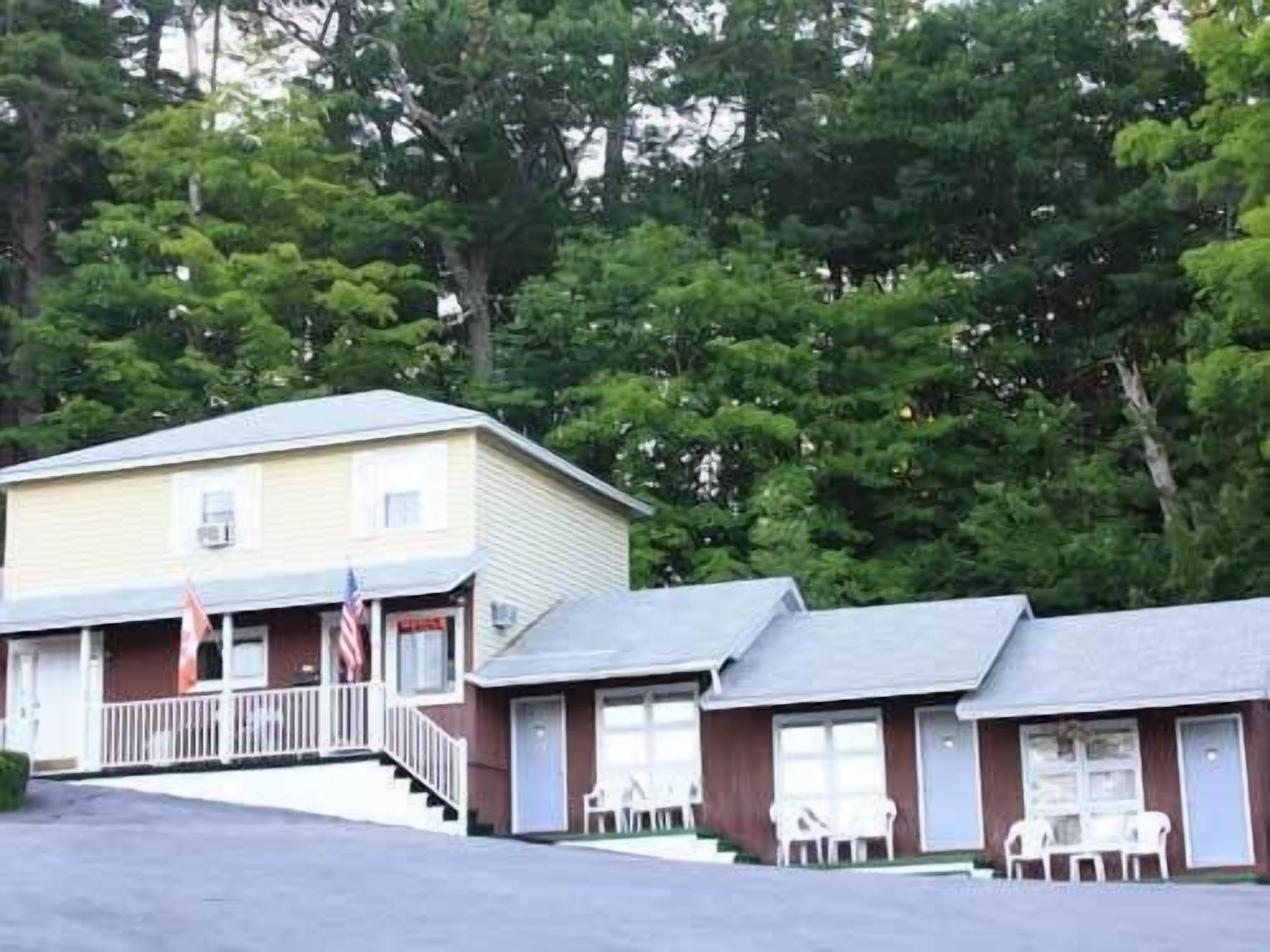 Un motel con un edificio central y dos unidades adosadas, cada una con un porche y mobiliario exterior.