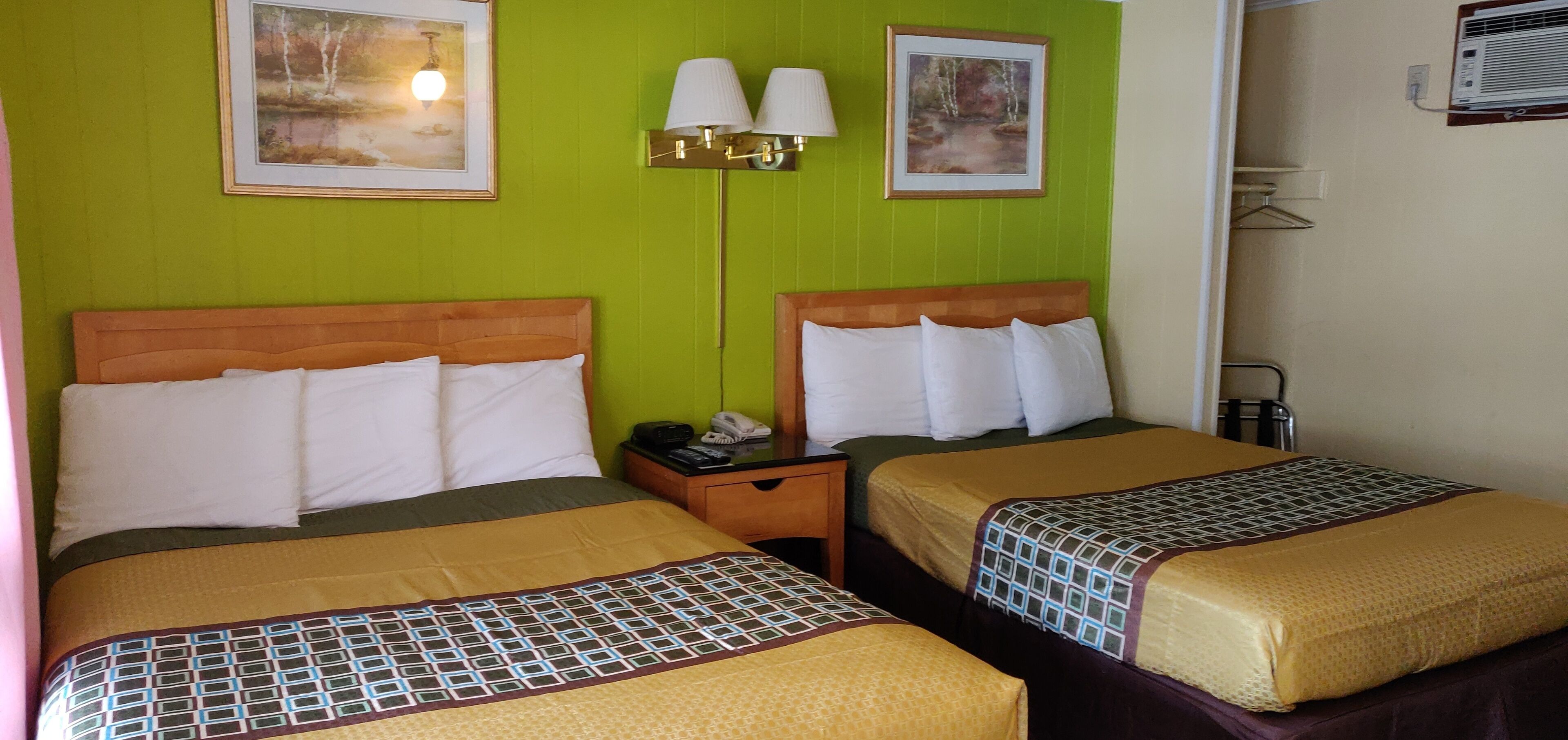 Ein Hotelzimmer mit zwei Betten, grünen Wänden, gerahmten Bildern, einem Nachttisch mit Lampe und einer Klimaanlage.