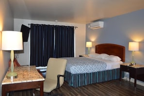 A hotel room with a bed, two bedside tables with lamps, a chair, a TV on the wall, and a window with curtains.