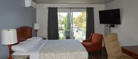 A hotel room with a bed, a chair, a TV, a lamp, and a balcony with a view.