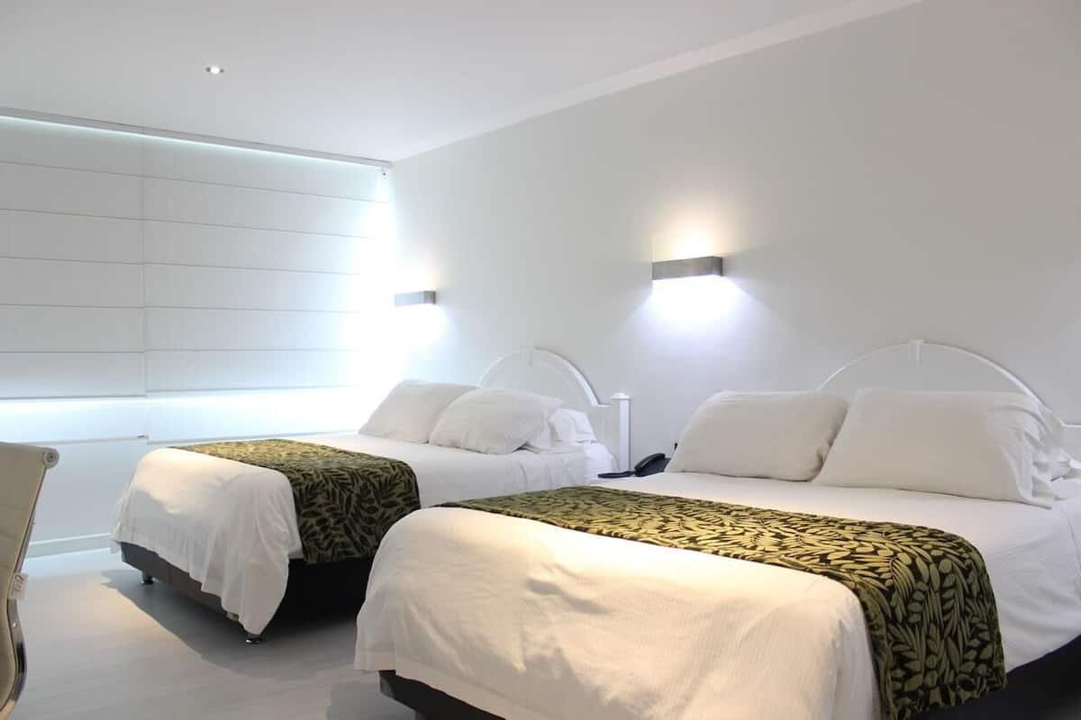 Habitación de hotel con dos camas, ropa de cama blanca y un ventanal grande.