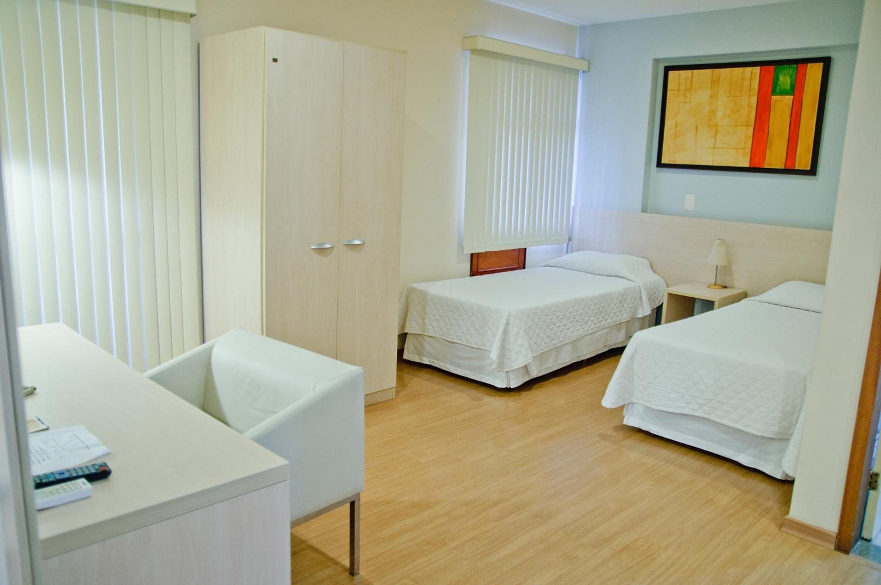 A hotel room with two single beds, a desk, a chair, and a wardrobe.