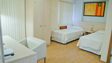 A hotel room with two single beds, a desk, a chair, and a wardrobe.