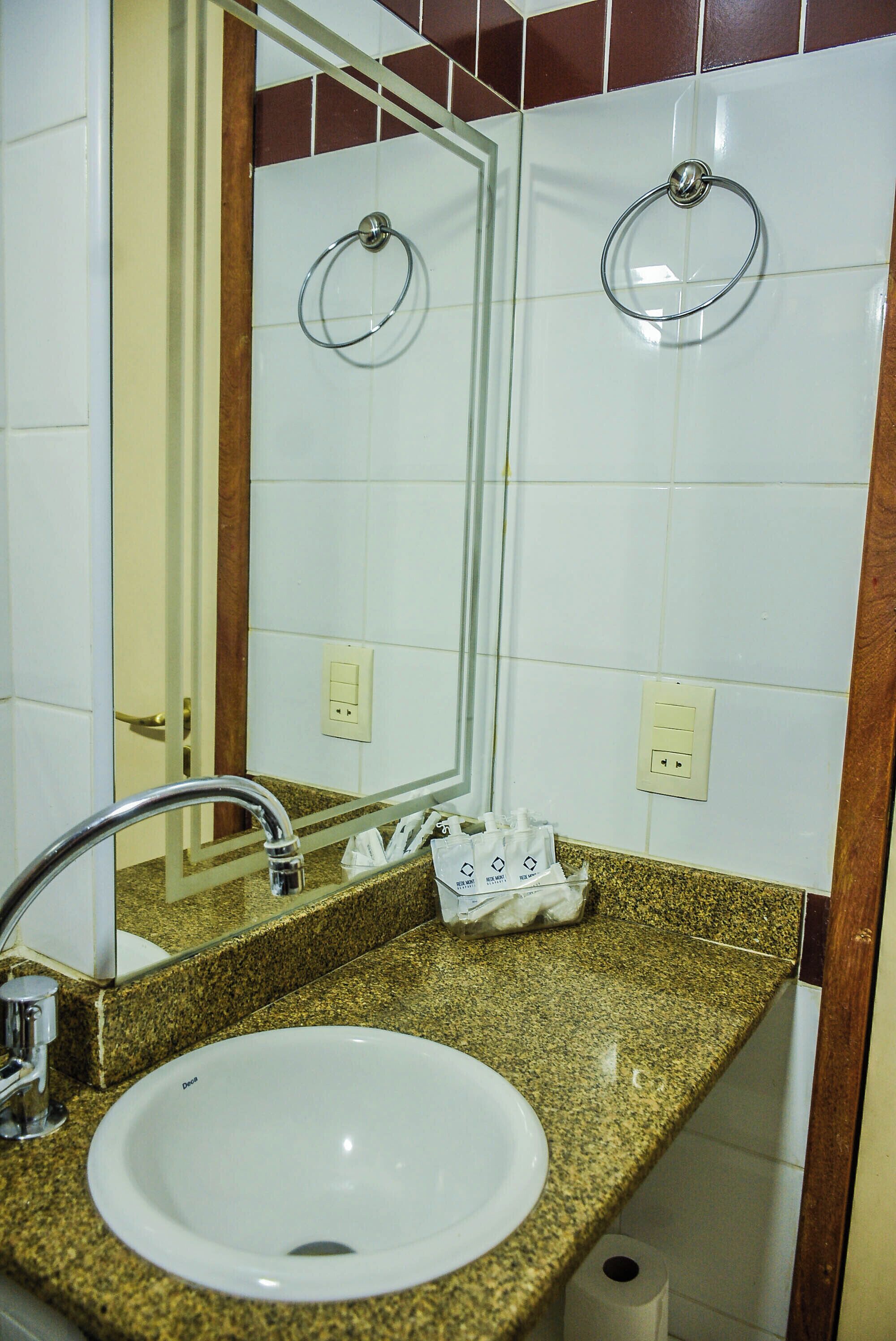 Un baño con encimera de granito, un lavabo blanco, un espejo y dos toalleros.