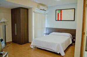 Un dormitorio con cama, armario, mesita de noche, lámpara y aire acondicionado.