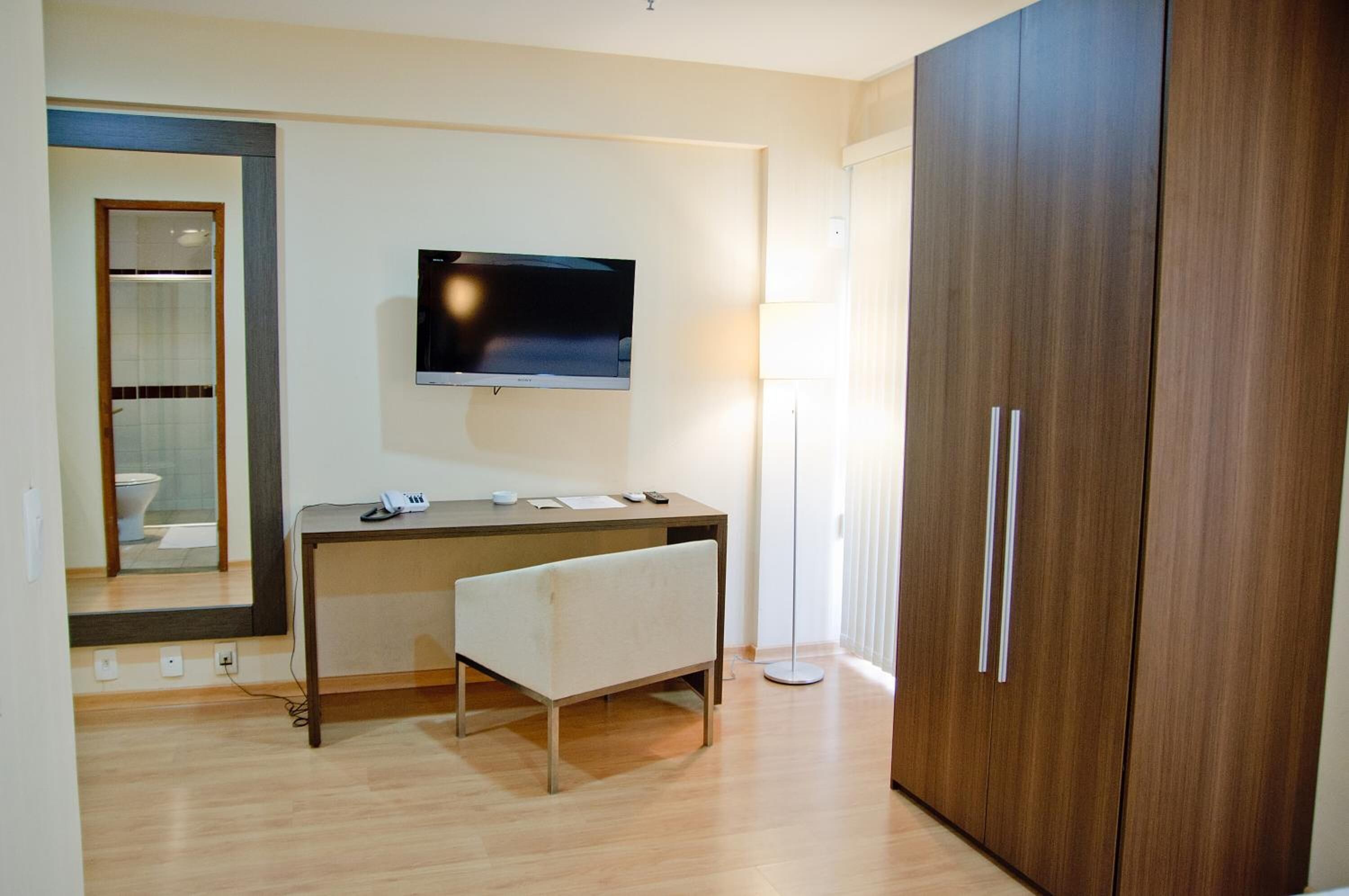 Una habitación moderna con un escritorio de madera, un televisor de pantalla plana, un banco y un armario.