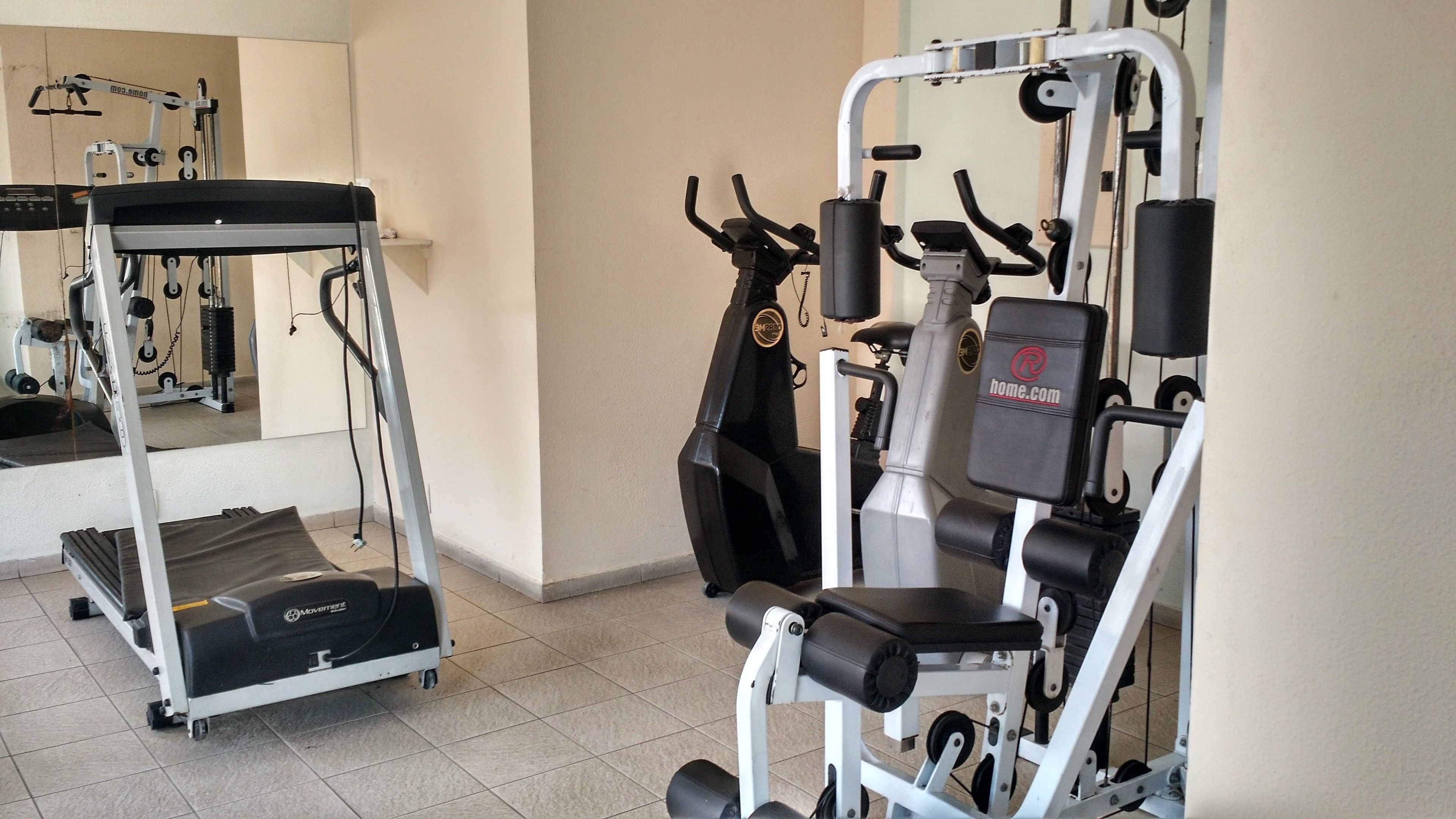 Een sportschool met cardioapparatuur, krachtapparaten en een spiegelwand.