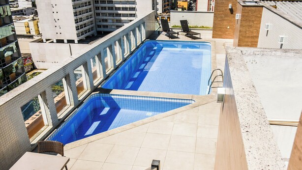 A rooftop swimming pool with a tiled deck, lounge chairs, and a table. - Mont Blanc Nova Iguaçu (Nova Iguaçu)