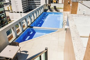 Ein Pool auf dem Dach mit gefliestem Sonnendeck, Liegestühlen und einem Tisch.