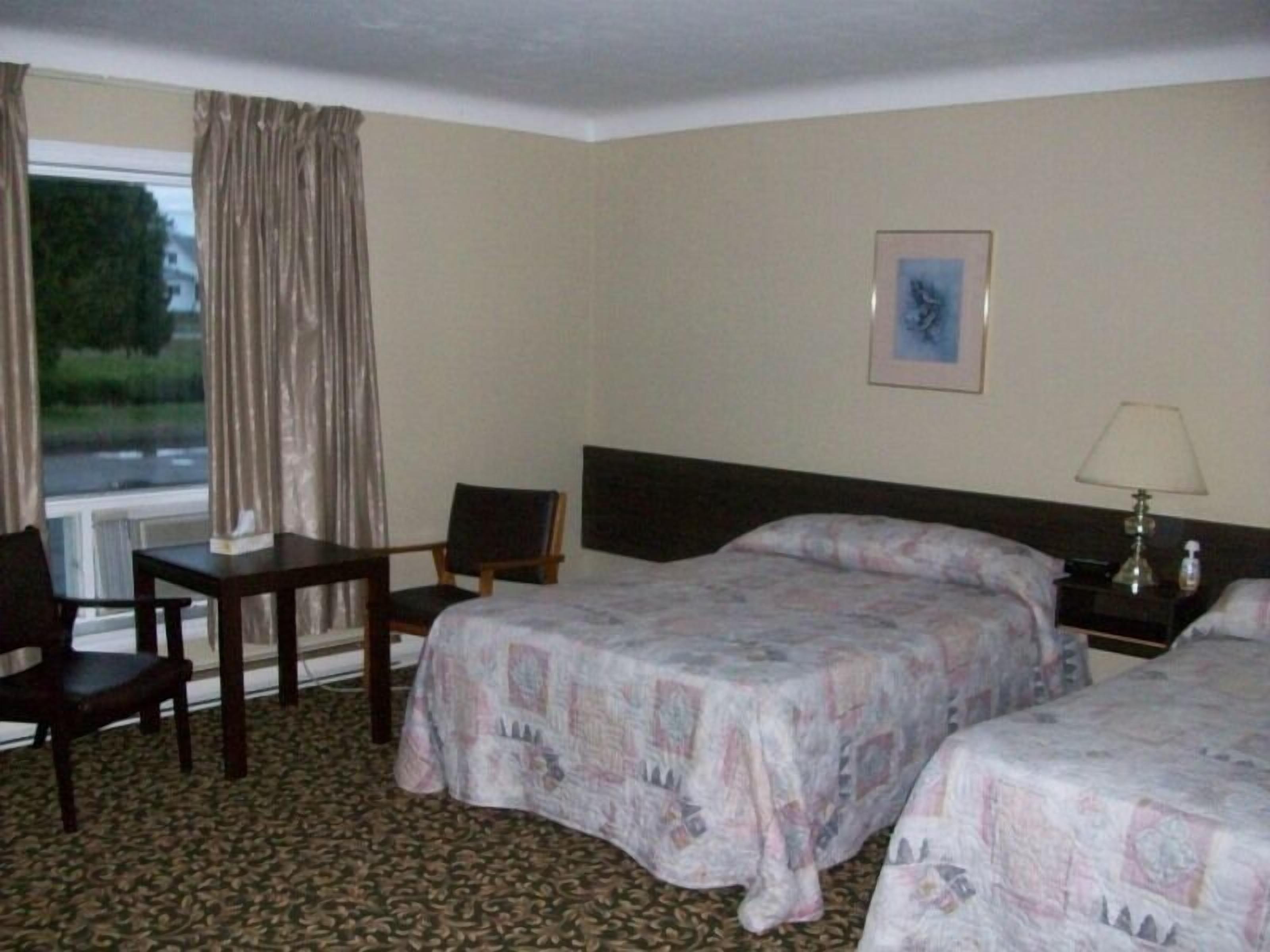 A hotel room with two beds, a desk, a chair, a nightstand with a lamp, and a window with curtains.