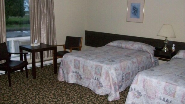 Habitación de hotel con dos camas, un escritorio, una silla, una mesita de noche con lámpara y una ventana con cortinas.
