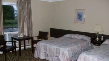 A hotel room with two beds, a desk, a chair, a nightstand with a lamp, and a window with curtains.