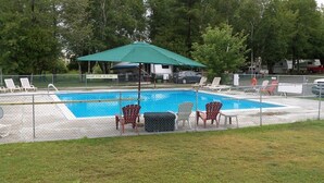Una piscina cercada con sillas de descanso y una sombrilla verde.
