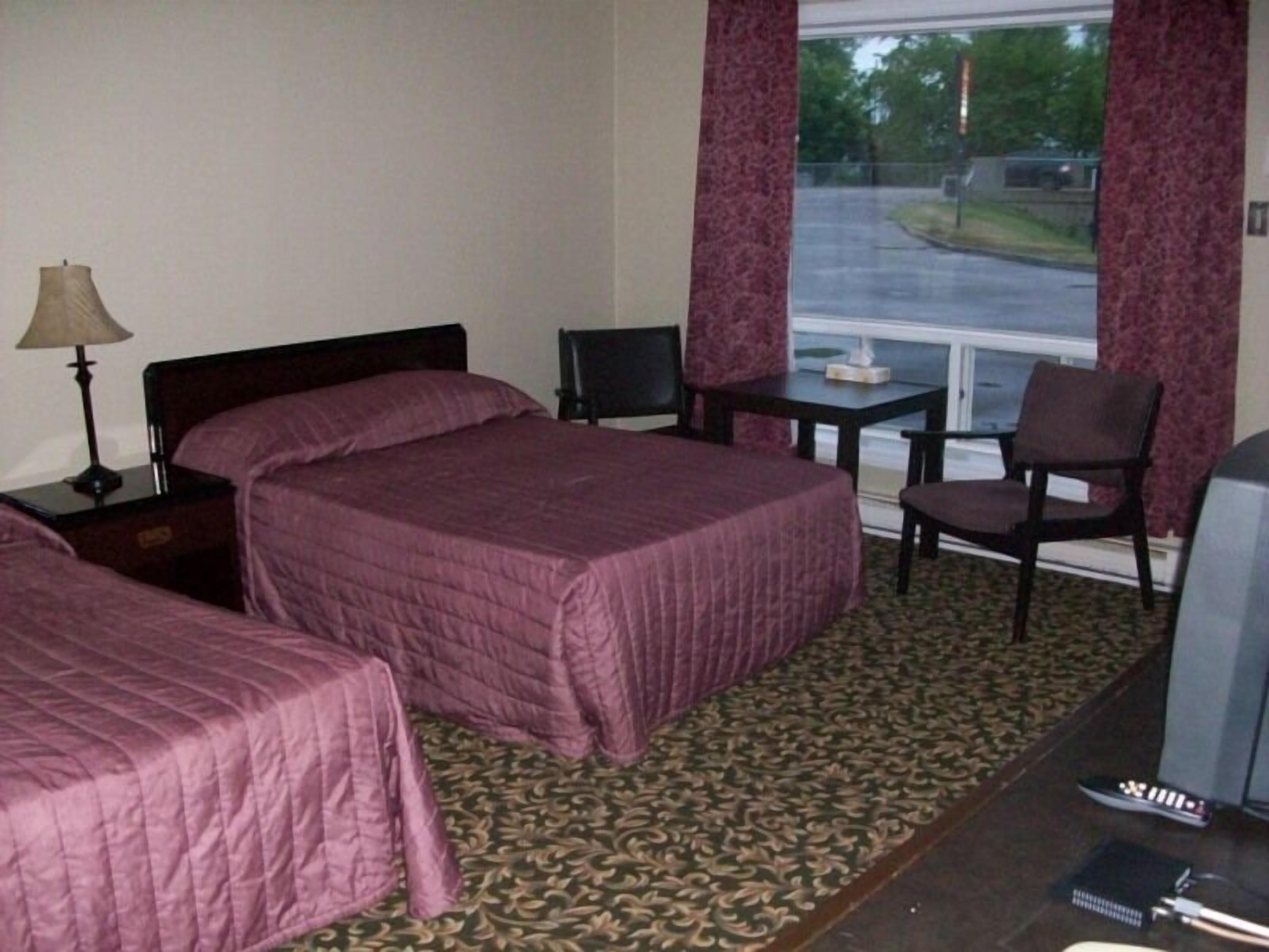 Une chambre d’hôtel avec deux lits, un bureau, une chaise, une télévision et une fenêtre donnant sur une route et des arbres.