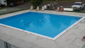 A rectangular swimming pool with a white edge, surrounded by a concrete deck. There are lounge chairs and a lifebuoy near the pool's edge.