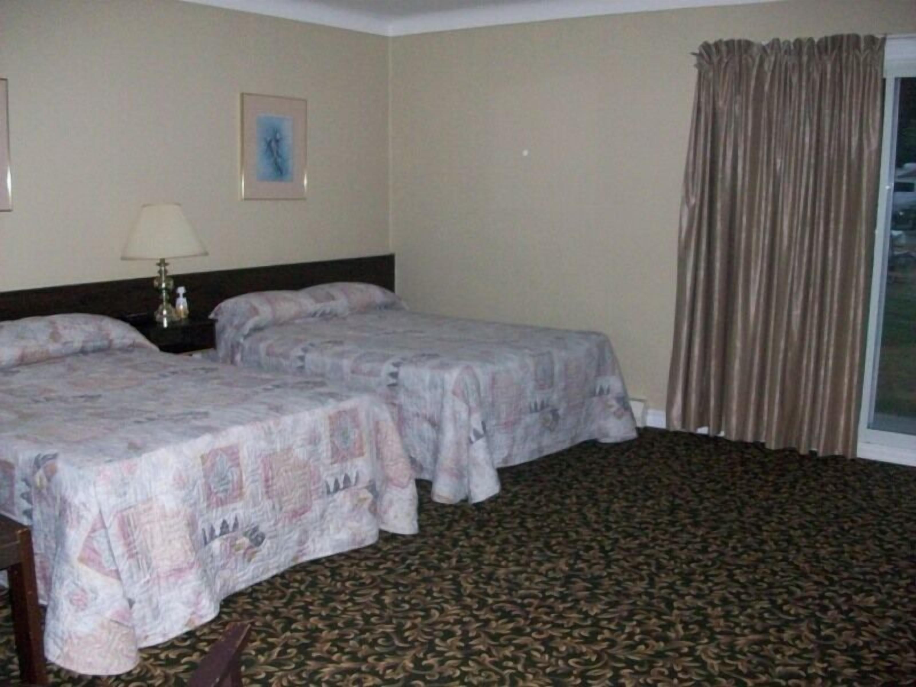 A hotel room with two beds, a nightstand, a lamp, a framed picture, and a window with curtains.