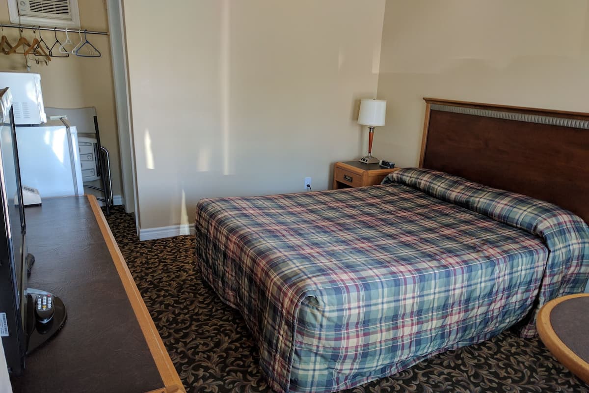 A hotel room with a bed, a desk, a lamp, and a dresser.
