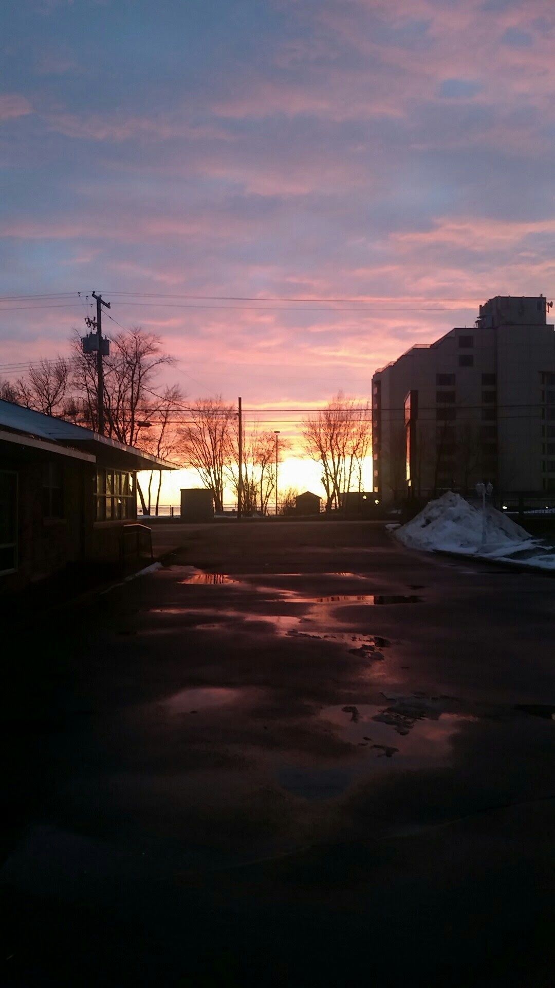 A parking lot with a building in the background and a sunset in the sky.