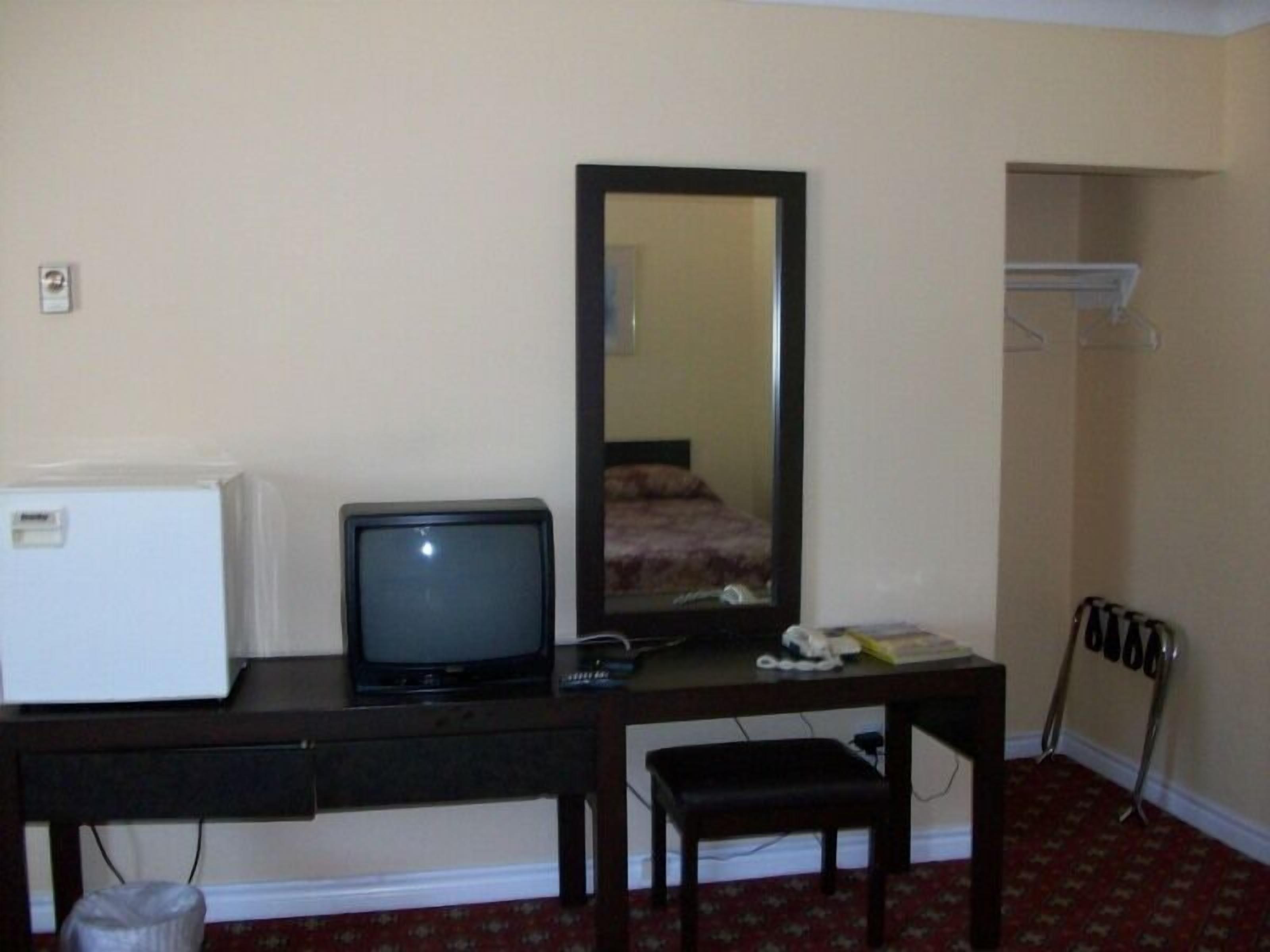 Ett hotellrum med ett skrivbord, en tv, en spegel, en liten pall och ett element.