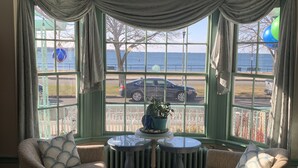 A cozy room with a view of the sea, featuring two armchairs, a round table, and a large window with curtains. - Harborview Inn (Gloucester)