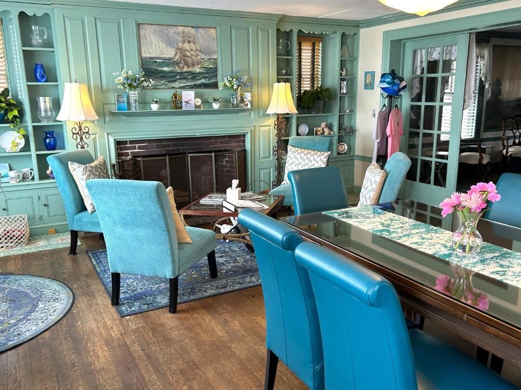 A room with a fireplace, blue chairs, a dining table, and a bookshelf.