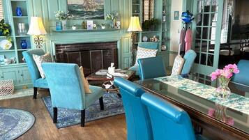 A room with a fireplace, blue chairs, a dining table, and a bookshelf.