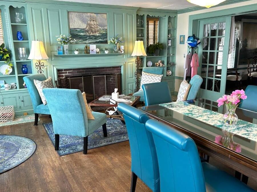 A room with a fireplace, blue chairs, a dining table, and a bookshelf.