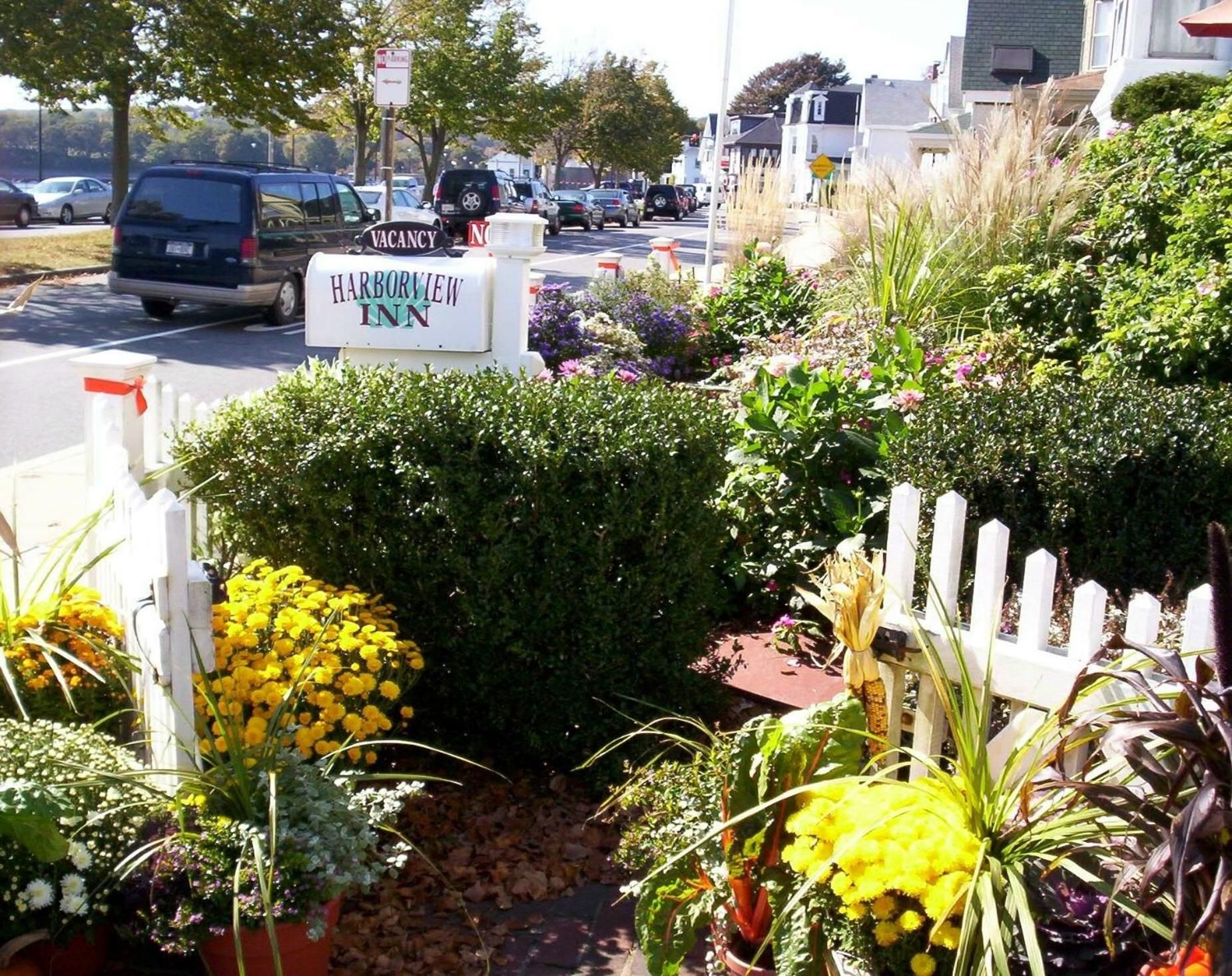 A street view with a sign for Harborview Inn, a white picket fence, and various potted plants.