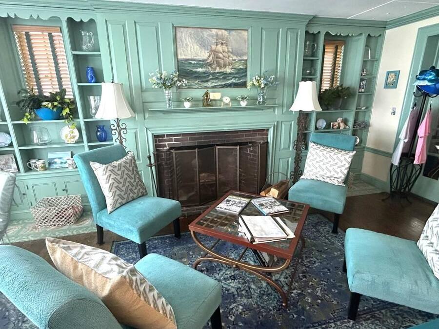 A room with teal-colored armchairs, a glass coffee table, a fireplace, and decorative items on shelves.