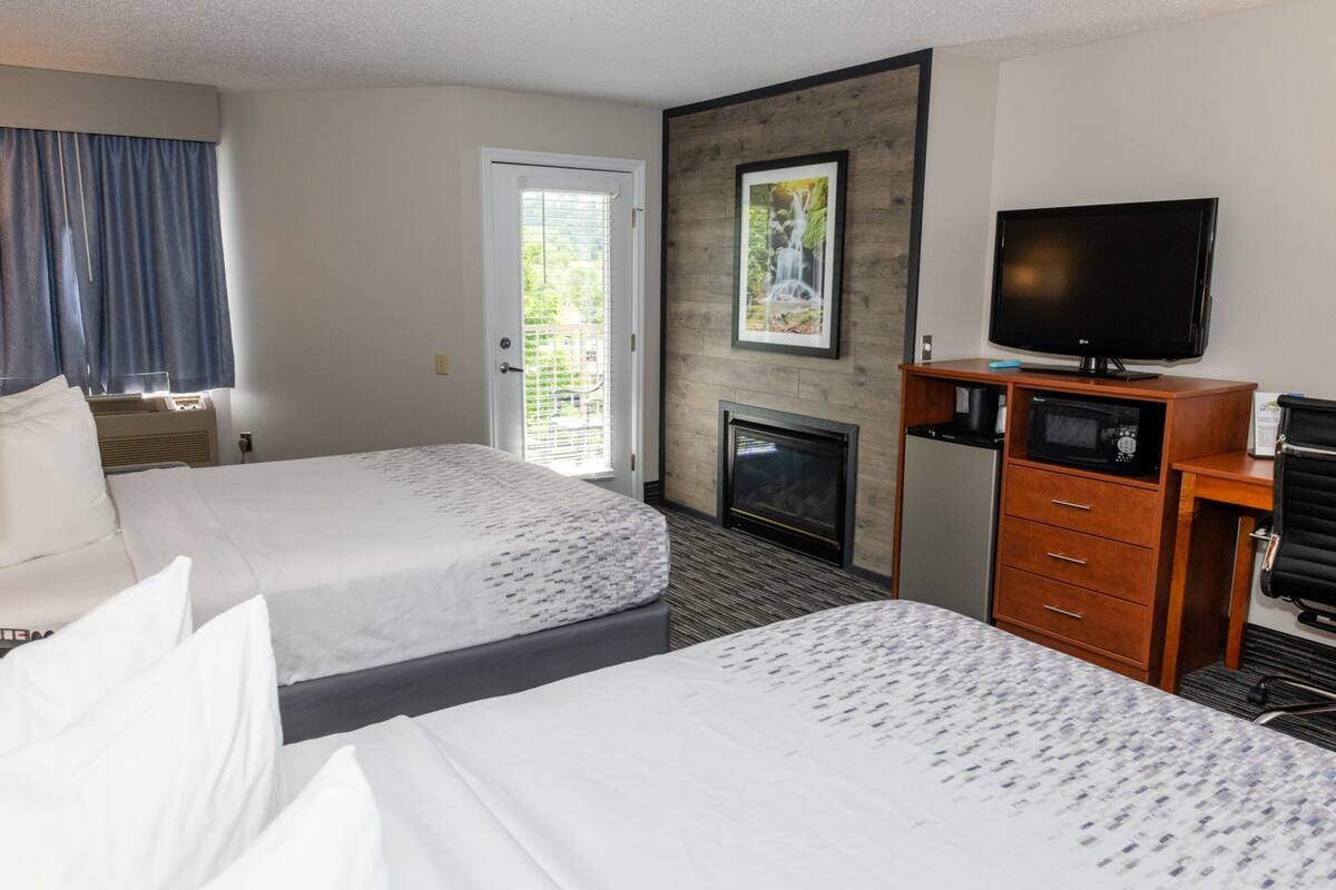 Quarto de hotel com duas camas, televisão, lareira e porta que dá para uma varanda.