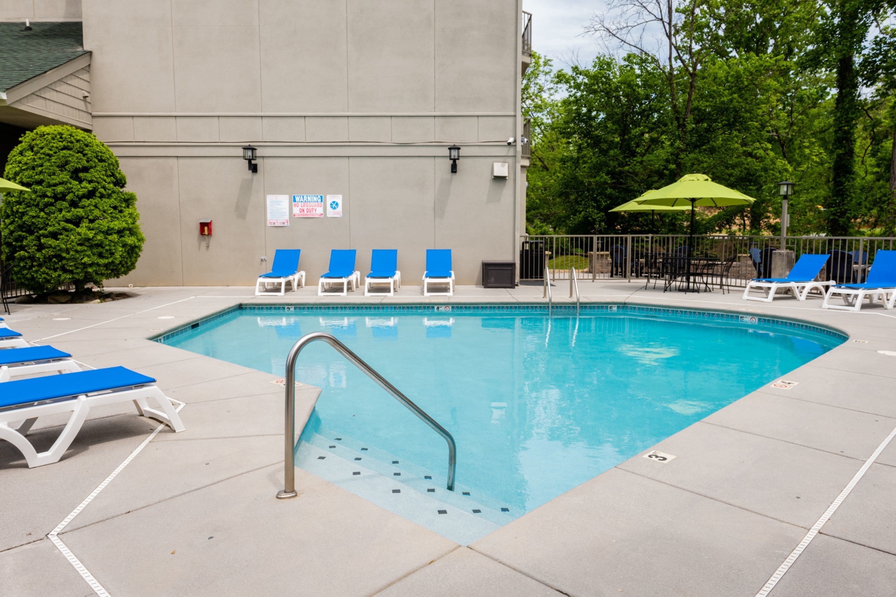 A swimming pool with blue lounge chairs and a green umbrella.